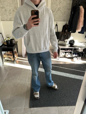 Ljusgrå basic hoodie med huva från pull and bear - En enkel och stilren ljusgrå hoodie med huva och magficka. Hoodien har ribbade muddar vid ärmslut och nederkant, samt en klassisk passform som funkar till det mesta. Perfekt för dig som gillar en clean och avslappnad look.