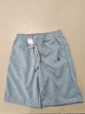 Ralph lauren shorts - Snygga grå sweatshorts med elastisk midja och dragsko. Shortsen har två sidofickor och en liten broderad logga på vänster ben. Tillverkade i mjukt sweatshirtmaterial som är perfekt för en avslappnad stil.