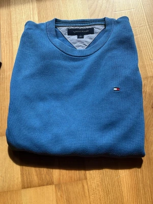 Blå tröja från Tommy Hilfiger - Snygg blå tröja från Tommy Hilfiger med rund halsringning och diskret logga broderad på bröstet. Tröjan är i mjukt material och har klassisk passform, perfekt för en clean och stilren look.