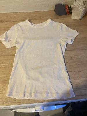 Vit ribbad t-shirt med kort ärm - En basic vit t-shirt med ribbad struktur och korta ärmar. Modellen är figurnära och har en klassisk rund halsringning. Perfekt att styla med jeans eller kjol för en enkel och clean look.