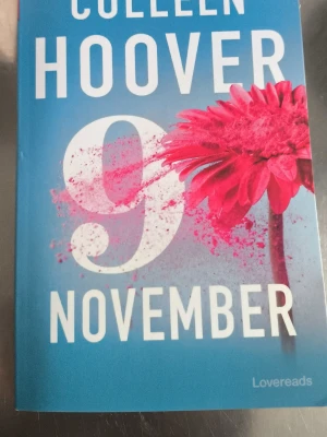 9 November av Colleen Hoover - En bok med blått omslag och stor vit text, skriven av Colleen Hoover. Omslaget har en stor siffra 9 och en rosa blomma med färgstänk. Perfekt för dig som gillar romantik och drama.