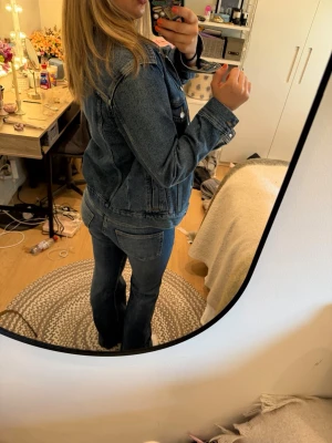 Klassisk blå jeansjacka - Säljer en klassisk blå jeansjacka i rak modell med knappstängning framtill och två bröstfickor med lock. Jackan har en tidlös look och passar perfekt till jeans eller andra outfits. Snygg att bära öppen eller stängd för en avslappnad stil.