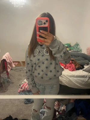 Dolce & Gabbana Grå hoodie med stjärnor och tryck - Säljer en grå hoodie med mörkblå stjärnor över hela tröjan och ett stort tryck på bröstet. Hoodien har huva och ribbade muddar vid ärmar och nederkant. Perfekt för dig som gillar en chill och trendig stil.