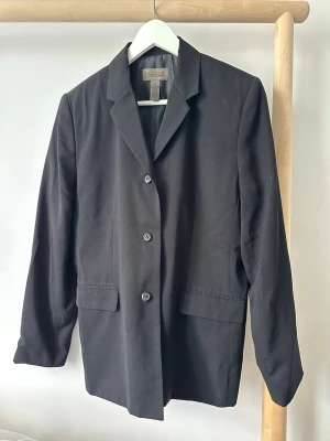 Svart klassisk kavaj med knappar - Stilren svart kavaj med tre knappar framtill och två fickor med lock. Klassisk krage och rak passform som ger en tidlös look. Storlek USA 12, vilket motsvarar runt storlek L.