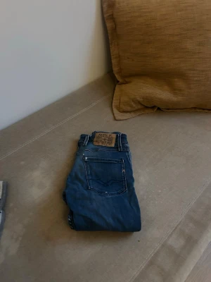 Blå raka jeans från replay - Säljer ett par klassiska blå jeans från replay med raka ben och femficksmodell. Jeansen har tydliga kontrastsömmar och en brun läderpatch bak i midjan. Materialet är slitstarkt denim i bomull mer har dock några slitningar därmed priset . Perfekta till en avslappnad stil.