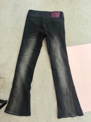Low waist jeans  - Säljer ett par svarta bootcut jeans med snygga slitningar och tvättade detaljer på benen. Jeansen har klassisk femficksmodell och låg midja. Materialet är denim med stretch för skön passform. Perfekta för en trendig och avslappnad look. Storleken är 28/32 vilket motsvarar s/m