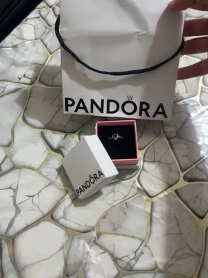 Pandora silverring med röd hjärtformad sten - Snygg silverring från Pandora med en röd hjärtformad sten i mitten och små klara stenar längs bandet. Ringen levereras i original ask och påse från Pandora. Perfekt för dig som vill ha en romantisk och elegant accessoar Den säljs eftersom köpte den till en speciell person men nu så är personen inte speciell längre.