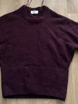 Vinröd stickad tröja Gina Tricot - Jag tog bort taggen för att det började klia. Mysig vinröd stickad tröja från Gina Tricot i ullblandning. Tröjan har hög hals, ribbstickade muddar och bred ribbad nederkant. Perfekt för kalla dagar och enkel att styla med jeans eller kjol.