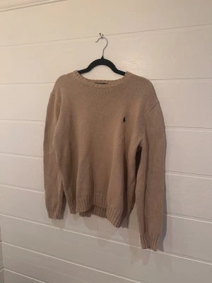 Polo Ralph Lauren beige stickad tröja storlek M - Säljer en beige stickad tröja med rund hals och långa ärmar. Tröjan har ribbade muddar vid ärmslut och nederkant samt en liten broderad logga på bröstet.