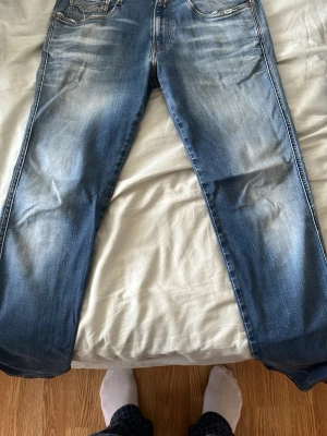 Replay Anbass jeans - Säljer ett par blå jeans med snyggt slitna detaljer och raka ben. Jeansen har klassisk femficksdesign och schyssta fades bak- och framtill för en cool look. Perfekta för dig som gillar en avslappnad stil. Slim fit.