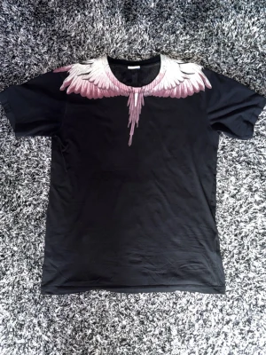 Marcelo Burlon t-shirt - Säljer en svart t-shirt från Marcelo Burlon med ikoniskt vingmönster i vitt och rosa runt halsen. T-shirten har rund hals och korta ärmar. Pris går att diskutera 