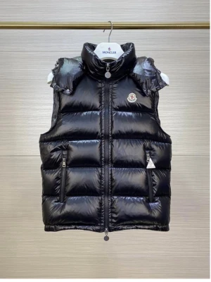 Svart dunväst med huva från Moncler - Snygg svart dunväst från Moncler med glansig finish och avtagbar huva. Västen har två dragkedjefickor framtill, quiltad design och klassisk Moncler-logga på bröstet. Perfekt för lager-på-lager och streetstyle. Ops medföljer en påse med olika tags 