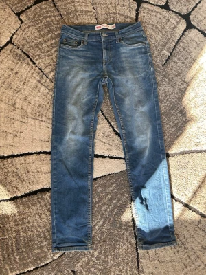 Levi's 502 Regular Taper jeans blå - Säljer ett par blå Levi's 502 Regular Taper jeans med klassisk femficksmodell och knappgylf. Jeansen har en snygg tvätt med slitningar och avsmalnande ben. Perfekta för en avslappnad och trendig look.