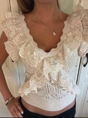 Vit spetsblus med volanger - Supersöt vit blus med spetsdetaljer och volanger. Toppen har v-ringning, korta ärmar och är croppad. Perfekt för dig som gillar romantisk och feminin stil. Materialet känns luftigt och mjukt.