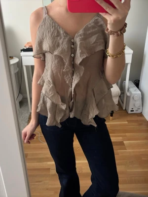 Beige volang topp med knappar - Säljer en beige linnetopp med knappar och volangdetaljer framtill. 