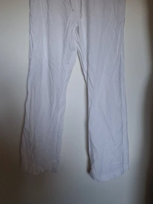 Vita vida linnebyxor med dragsko - Säljer ett par vita linnebyxor med avslappnad passform och dragsko i midjan. Byxorna har raka, vida ben och är tillverkade i ett lätt och luftigt linnematerial. Perfekta för en chill och stilren look.