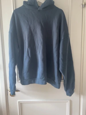 Blå hoodie från Acne Studios - Säljer en oversized blå hoodie från Acne Studios med tryck på ryggen där det står 'Acne Studios STOCKHOLM 1996'. Hoodien har luva, ribbade muddar och är gjord i mjukt bomullsmaterial. Perfekt för en chill och trendig look.