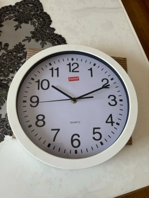 Vit väggklocka från Staples - Stilren rund väggklocka med vit ram och svart urtavla från Staples. Klockan har tydliga svarta siffror och visare samt en sekundvisare. Drivs med batteri och har upphängningsfäste på baksidan. Perfekt för kök, kontor eller vardagsrum.