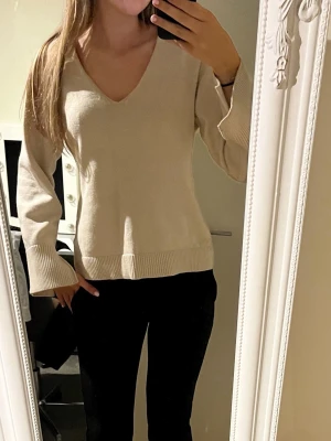 Beige stickad tröja med v-ringning - Beige stickad tröja med  v-ringning och vida ärmar. Tröjan är nopprig på vissa ställen och på insidan så är den lite blå då mina jeans har färgat av sig. Vid funderingar skriv och priset kan diskuteras.✨💕