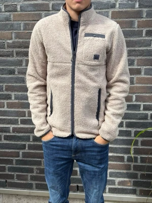 Beige teddyjacka med dragkedja - Mysig beige teddyjacka med hög krage och hel dragkedja framtill. Jackan har två fickor med svarta dragkedjor och en liten bröstficka med detalj. Perfekt för kalla dagar och riktigt skön att ha på sig.. Skriv gärna vid frågor! Modell:180/70kg