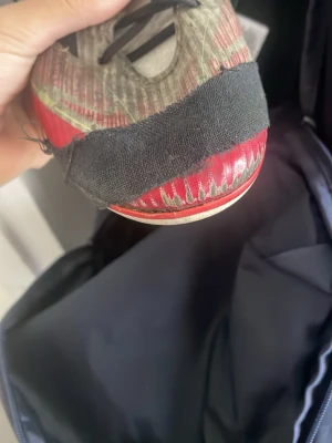 Adidas vita och röda fotbollsskor - Säljer ett par snygga Adidas fotbollsskor med vit bas, röda och gula detaljer samt svarta ränder på sidan. Skorna har röda snören och en låg profil för bra bollkontroll. Ovandelen är i syntetmaterial och sulan är anpassad för spel på gräs. Den har hål på fram vid tårna 