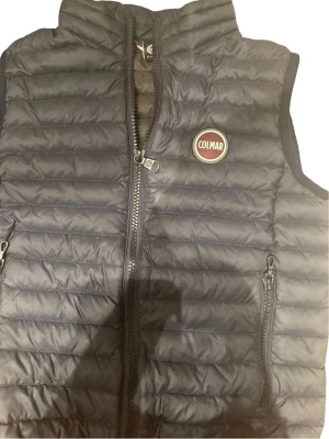 Mörkblå dunväst från Colmar - Snygg mörkblå dunväst från Colmar med quiltad design och två dragkedjefickor framtill. Västen har hög krage och Colmar-logga på bröstet. Perfekt för lager-på-lager och håller dig varm under kyliga dagar. 