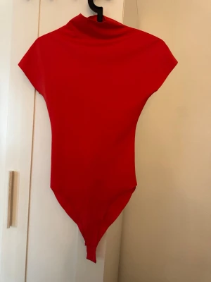 Röd body med polokrage - Snygg röd body med hög polokrage och korta ärmar. Tillverkad i ett stretchigt material som sitter tight mot kroppen. Perfekt att styla med jeans eller kjol för en trendig look.