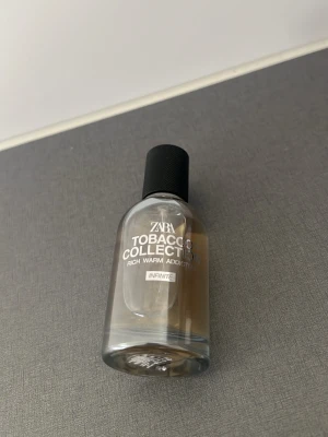 Zara Tobacco Collection Infinite parfym - Zara Tobacco Collection Infinite är en parfym med varm och rik doft. Flaskan är genomskinlig med en svart kork och har en stilren, modern design. Texten på flaskan är vit och tydlig. Perfekt för dig som gillar unika och djupa dofter.