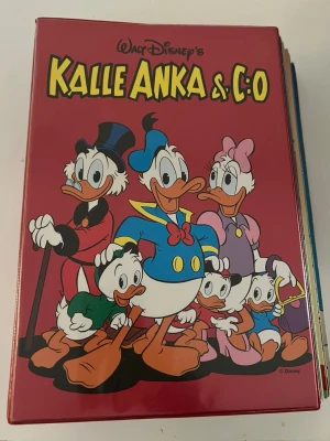 Kalle Anka & C:o samlingsvolym - Säljer en samlingsvolym av Walt Disney's Kalle Anka & C:o med röd hård pärm. Omslaget pryds av Kalle Anka, Knattarna, Farbror Joakim och Kajsa Anka i färgglada kläder. Perfekt för dig som gillar klassiska serier och Disney.