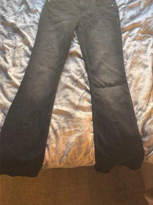 Svarta bootcut jeans - Säljer ett par svarta bootcut jeans med klassisk femficksdesign. Jeansen har utsvängda ben och normal midja. Materialet ser ut att vara denim med en lätt tvättad look. Perfekta för dig som gillar retrostil och vill ha ett par bekväma jeans med snygg passform.