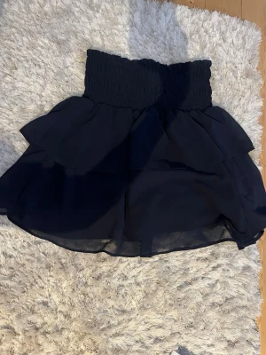 Svart volangkjol med smock - Kort svart kjol med bred smock i midjan och dubbla volanger. 