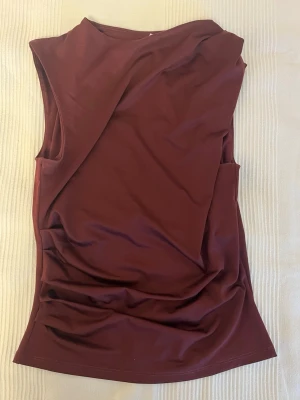 Vinröd ärmlös topp från Divided - Snygg vinröd ärmlös topp från Divided by H&M. Toppen har en enkel, clean design med rund hals och är tillverkad i ett mjukt, stretchigt polyestertyg. Perfekt att styla med jeans eller kjol för en trendig look.