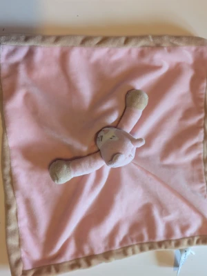 Rosa snuttefilt med katt teddykompaniet  - Mysig snuttefilt i rosa med beige kant och en mjuk katt i mitten. Filten är fyrkantig och tillverkad i mjukt tyg, perfekt som gosedjur eller trygghetsfilt för små barn.