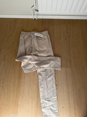 Beige linnebyxor med resårmidja - Snygga beige linnebyxor med rak passform och resår i midjan. Byxorna har en enkel och stilren look, perfekta för en avslappnad och trendig stil. Tillverkade i ett lätt och luftigt linnematerial som passar bra till varmare dagar.
