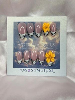 Fauve (S);Medium Almond - Snygga handgjorda press-on naglar i en medium lång mandelform med nude bas och med vit handmålad french, med zebramönstrade tippar. Två naglar har handgjorda 3D-blommor i gult/orange med pärldetaljer. Perfekt för dig som vill sticka ut med en unik och trendig nageldesign.S: 15 mm, 11,5 mm, 12 mm, 11 mm, 9 mm 