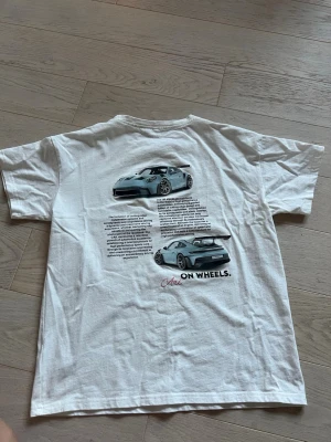 Vit t-shirt porsche - Vit t-shirt med tryck på ryggen. Strl M men sitter som strl S. Endast provad satt nyskick, säljer för att den satt för tajt. 