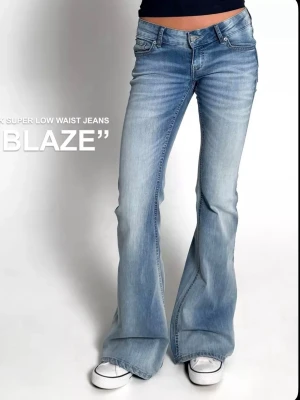 Blå bootcut jeans med låg midja - Säljer ett par ljusblå bootcut jeans med superlåg midja och klassisk femficksmodell. Jeansen har en snygg tvättad look och vida ben som ger en retro vibe. Perfekta för dig som gillar 00-talsstilen och vill ha ett par riktigt trendiga jeans.