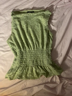 Grön spetsblus från Gina Tricot - Säljer en ljusgrön blus från Gina Tricot i spets med smockad midja och volang nedtill. Blusen är ärmlös och har ett blommigt spetsmönster som ger en romantisk vibe. Perfekt att styla med jeans eller kjol.