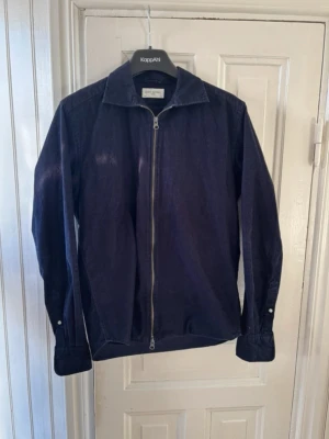 Marinblå manchester overshirt från John Henric - Stilren marinblå overshirt från John Henric i mjuk manchester. Jackan har hel dragkedja framtill, klassisk krage och knapp vid ärmslut. Perfekt lager på lager-plagg för en avslappnad men snygg look.