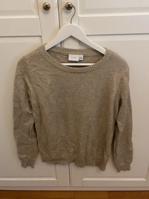 Beige stickad tröja från VILA - Mysig beige stickad tröja från VILA med rund halsringning och ribbade muddar vid ärmslut och nederkant. Perfekt för lager på lager och enkel att matcha med olika outfits. Klassisk och stilren design som passar till det mesta. Den är så mysig och perfekt inför hösten