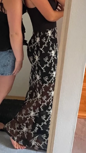 Svart långkjol med vit brodyr - Säljer en svart långkjol med transparent tyg och vit broderad blommönster. Kjolen har en flowy passform och är perfekt för sommarens alla tillfällen. Tunt material som ger en luftig känsla och snygg kontrast mellan svart och vitt.