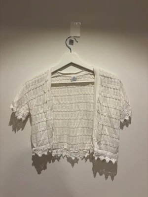 Vit virkad bolero från Lindex - Söt vit kortärmad bolero från Lindex i virkad stil med fina spetsdetaljer längs kanterna. 