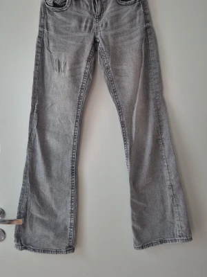 Grå bootcut jeans från Gina Tricot - Säljer ett par grå bootcut jeans från Gina Tricot i storlek 158. Jeansen har två knappar framtill, klassisk femficksmodell och en snygg tvättad look. Perfekta för dig som gillar en avslappnad men trendig stil.