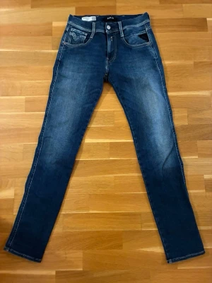 Mörkblå replay jeans - Snygga mörkblå jeans från replay modellen heter hyper flex med klassisk femficksdesign och kontrastsömmar. Jeansen har en lätt tvättad look med slitningar på låren och smal passform hela vägen ner. Perfekta för en trendig och avslappnad stil. Storlek W29 L32 med passform anbass 