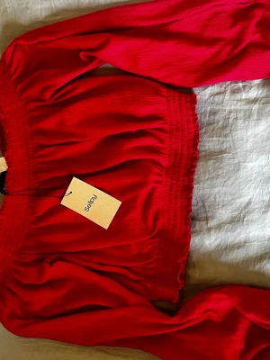 Röd off shoulder topp med puffärm - Trendig röd off shoulder topp med långa puffärmar och smockdetaljer vid halsringning och midja.  Går även att vika upp för att få den som en ballong tröja 