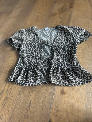 En snygg blus - Säljer en kortärmad topp med leopardmönster i färgen beige och brun. Toppen har v-ringning, liten knytning framtill och volangkant nedtill. Materialet är stretchigt och bekvämt.