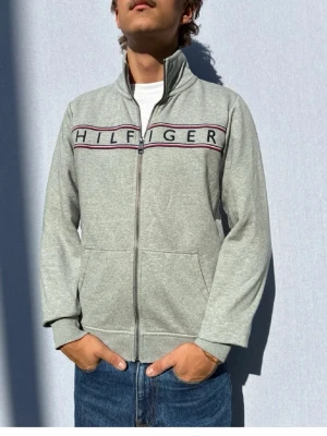 Grå ziptröja från Tommy Hilfiger - Hej och välkommen till byTorén. Detta är en kofta från Tommy Hilfiger i storlek S med normal passform. Modell på bild är ca 182, 67kg. Plagget är i bra skick utan några defekter. Tveka inte på att höra av dig, även om det skulle vara minsta lilla;)