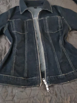 Mörkblå figursydd jeansjacka - Snygg mörkblå jeansjacka med markerade vita sömmar och figursydd passform. Klassisk krage och långa ärmar. Perfekt för dig som vill ha en tidlös och trendig jacka i garderoben. I väldigt fin skick storlek M