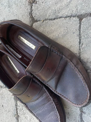 Bruna loafers i läder från Kemal Tanca - Snygga bruna loafers i äkta läder från Kemal Tanca. Skorna har perforerat mönster över hela ovandelen och klassisk pennyloafers-design med dekorativ söm runt tån. Perfekta för en stilren och avslappnad look.