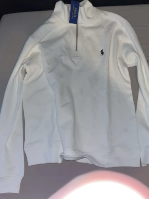 Polo Ralph Lauren Quarter zip  - Klassisk vit långärmad halvzip från Polo Ralph Lauren med broderad marinblå logga på bröstet. Tröjan har hög krage och dragkedja framtill. Tillverkad i mjukt material som känns skönt mot huden.